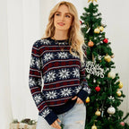 Woman wearing a navy blue holiday sweater with a snowflake pattern, standing in front of a Christmas tree.