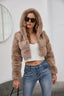 Woman wearing a cropped faux fur hooded jacket over a white camisole and blue jeans, front view.