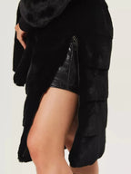 Close-up of the zipper detail on the side of a black faux fur coat.