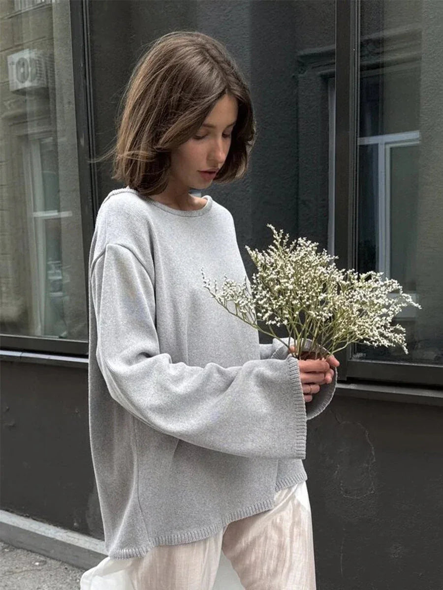 Woman wearing an oversized grey knit sweater with wide bell sleeves and a white skirt, holding a bouquet of dried flowers. Main image
