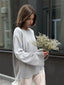 Woman wearing an oversized grey knit sweater with wide bell sleeves and a white skirt, holding a bouquet of dried flowers.