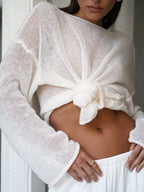 Close-up of a woman wearing a white sheer knit sweater tied at the waist, revealing her midriff.