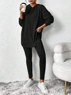 Woman in a black ribbed knit loungewear set, one hand in pocket, holding a coffee cup.