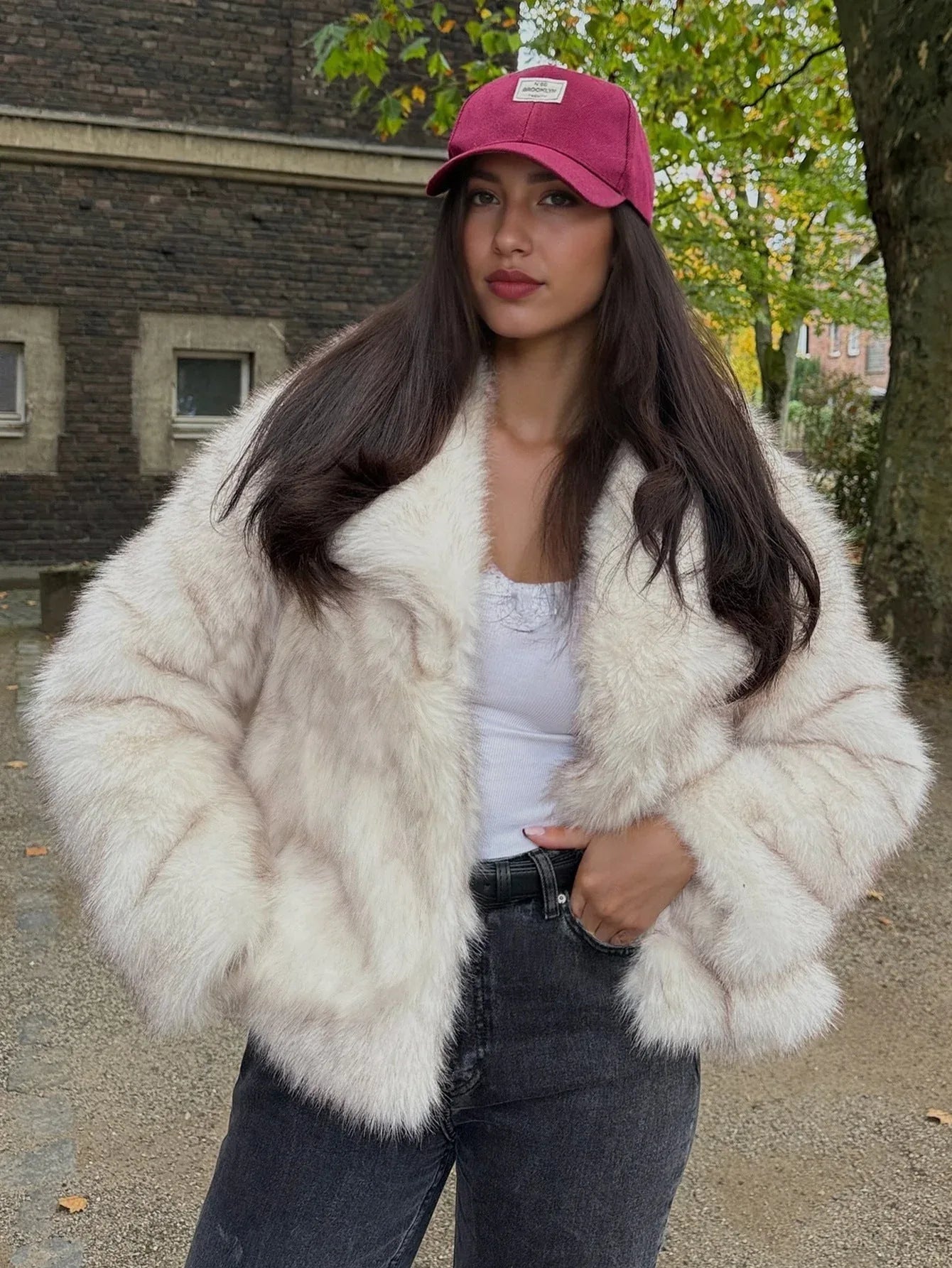 Woman in a cream faux fur jacket and pink baseball cap, posing outdoors.
