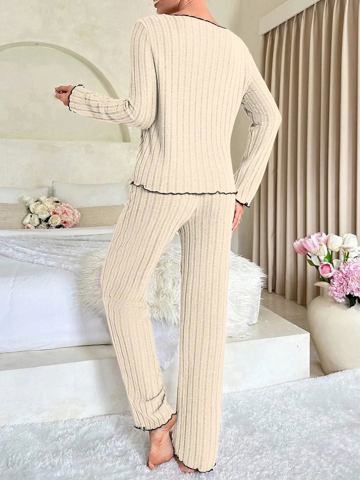 Back view of a woman wearing a cream ribbed knit pajama set with black trim.