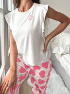 Close-up of a woman's torso wearing a white pajama top with a pink ribbon graphic and white pants with a pink heart print.