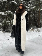 Woman wearing a long black and white faux fur coat and black pants, standing in a snowy forest.