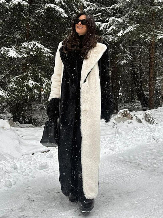 Woman wearing a long black and white faux fur coat and black pants, standing in a snowy forest.