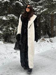 Woman wearing a long black and white faux fur coat and black pants, standing in a snowy forest.