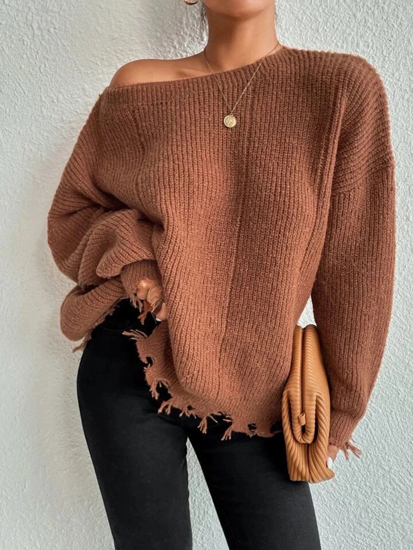 Woman wearing a rust-colored oversized distressed knit sweater with black pants, a necklace, and a clutch