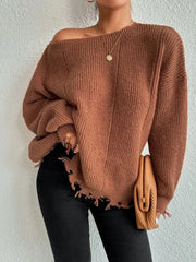 Woman wearing a rust-colored oversized distressed knit sweater with black pants, a necklace, and a clutch