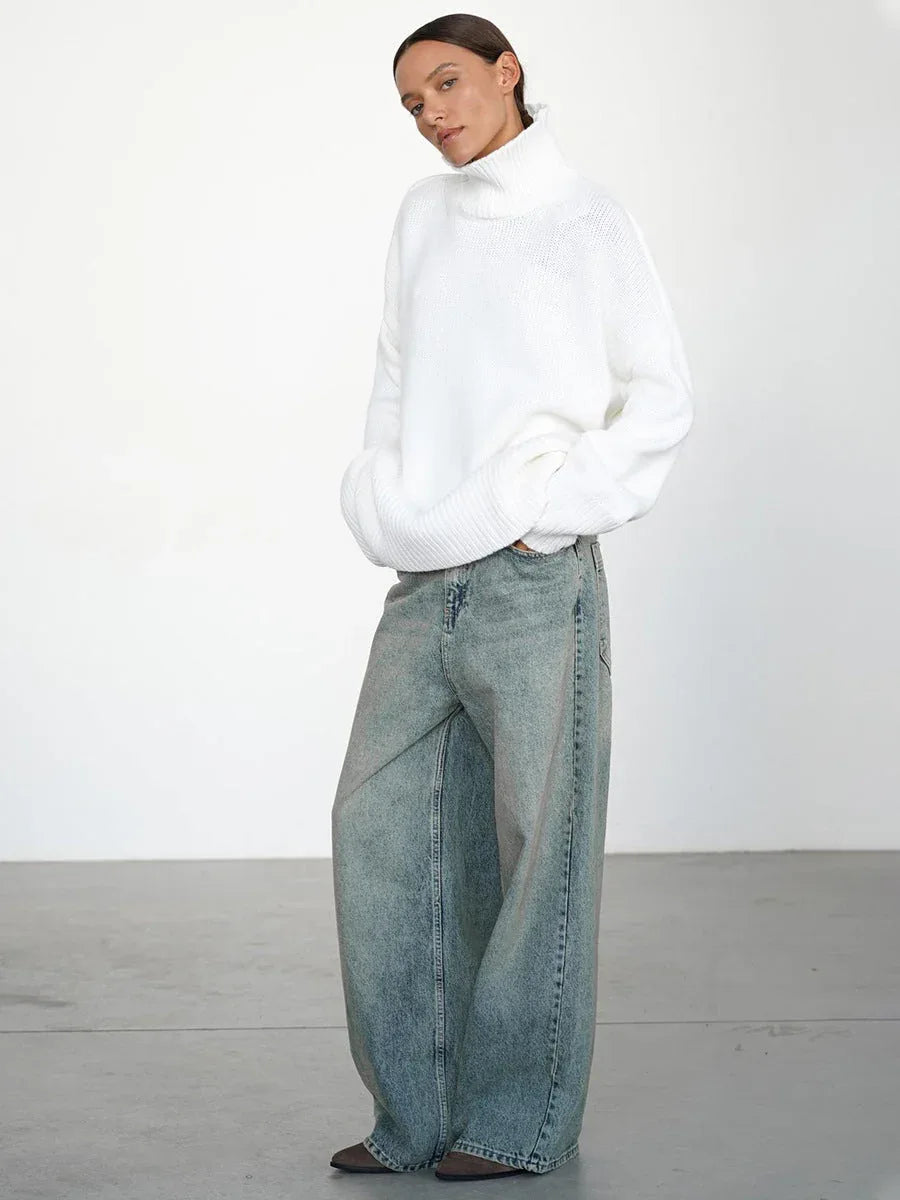 Side view of a woman wearing an oversized white turtleneck sweater and wide-leg blue jeans.