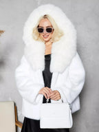 Woman wearing a white faux fur short coat with a hood and sunglasses, holding a white handbag