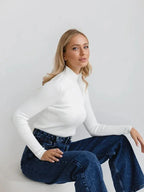 Close-up of a woman wearing a white ribbed mock neck cropped sweater and dark wash wide-leg jeans.