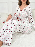 Woman wearing white pajamas with red heart print, sitting on a bed.
