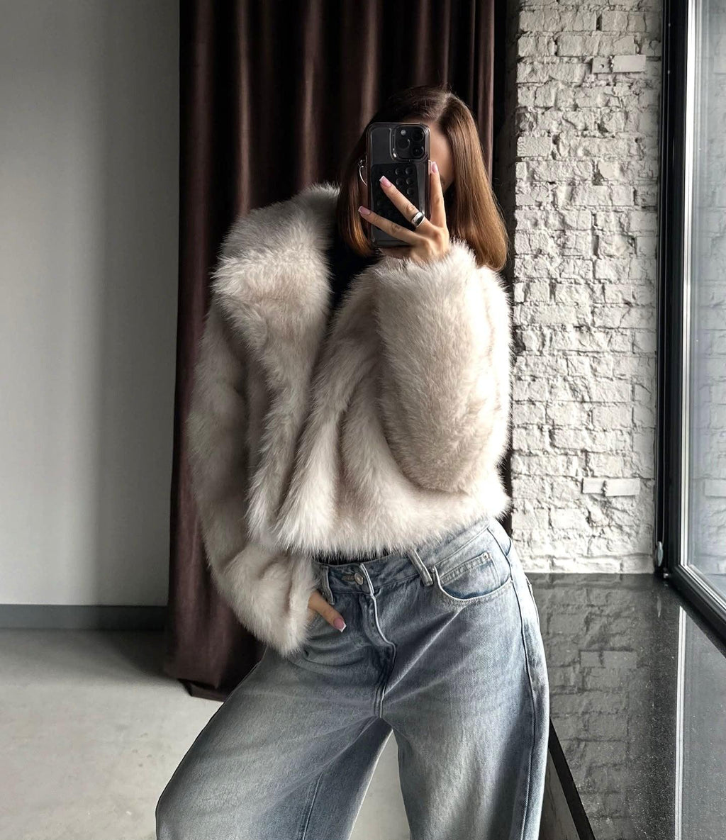 Side view of a woman in a cream faux fur cropped jacket and light wash wide-leg jeans, holding a phone to take a mirror selfie.