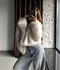 Side view of a woman in a cream faux fur cropped jacket and light wash wide-leg jeans, holding a phone to take a mirror selfie.