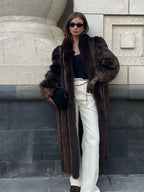 full body shot of a woman in a chic brown fur coat and white flared pants