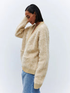 Side view of a woman wearing a beige fuzzy V-neck button-up cardigan with two front pockets.