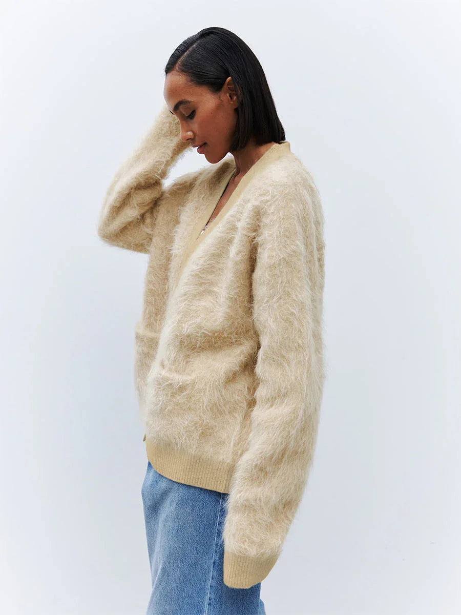 Side view of a woman wearing a beige fuzzy V-neck button-up cardigan with two front pockets.