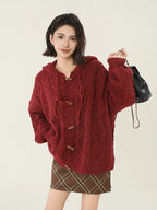 Woman holding a black backpack while wearing a burgundy cable knit hooded cardigan.