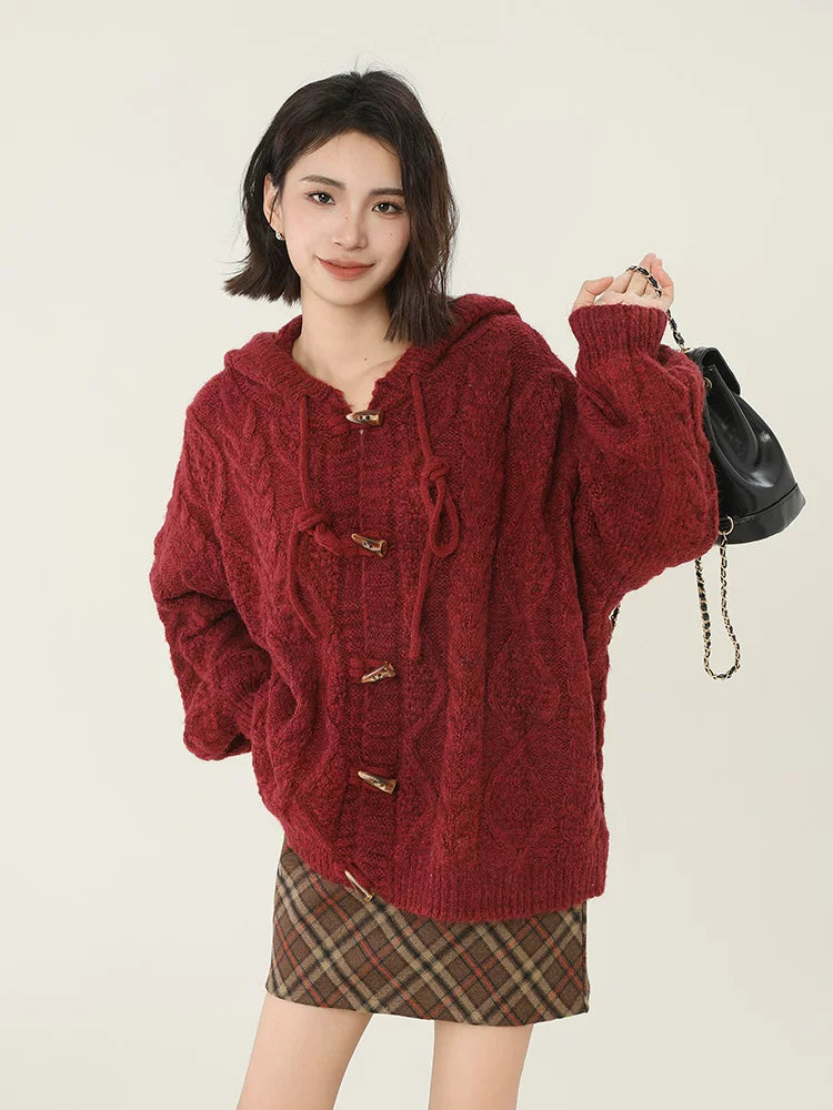 Woman holding a black backpack while wearing a burgundy cable knit hooded cardigan.