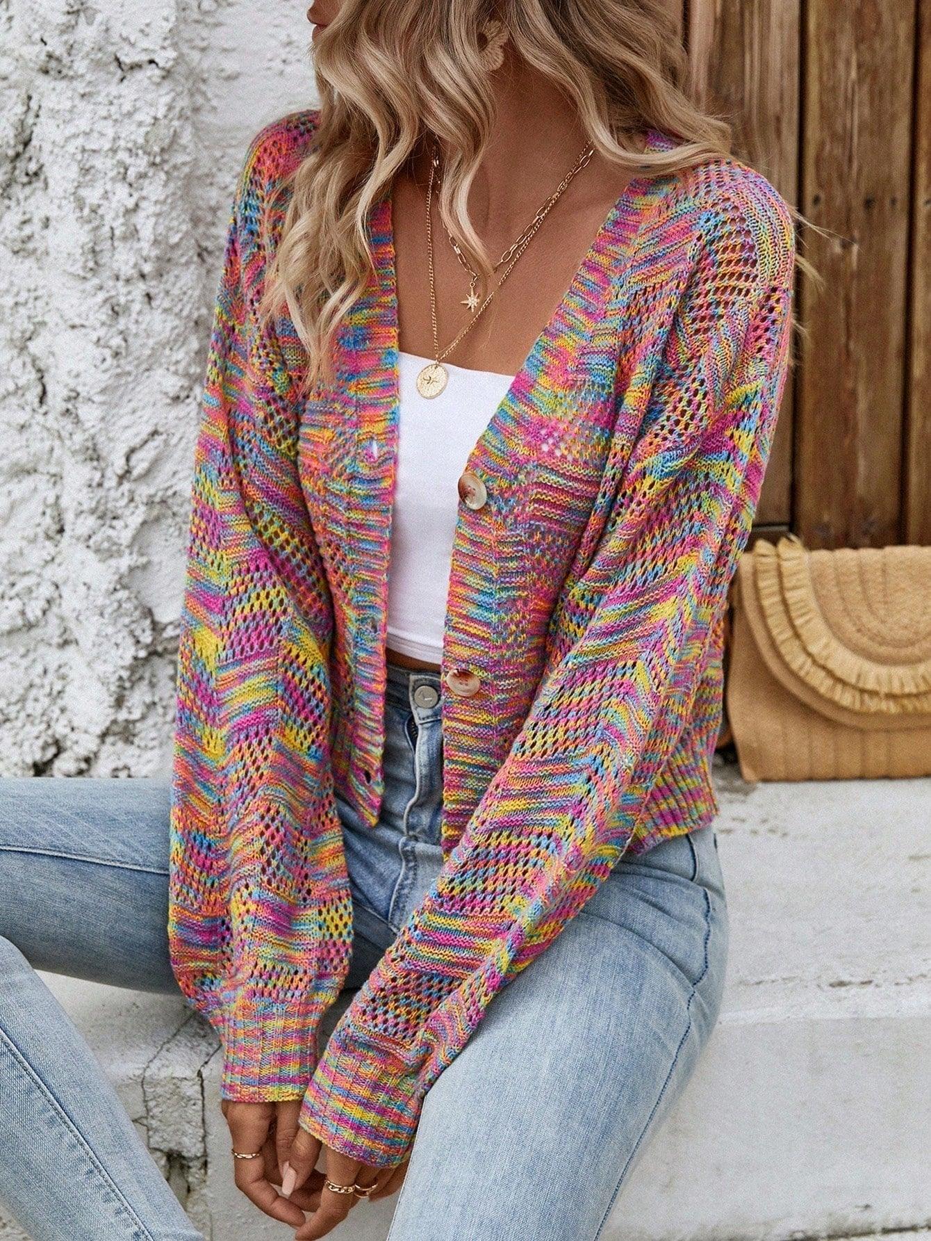 Woman sitting outdoors wearing a multicolor rainbow knit cropped cardigan, white top, and blue jeans.