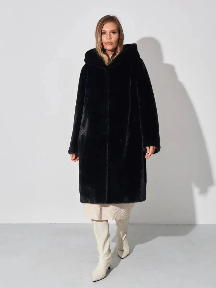 Woman wearing a black hooded faux fur coat, cream dress, and white boots, front view.