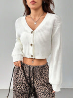 Close-up of a woman wearing a white cropped knit cardigan, leopard print pants, and a heart pendant necklace.