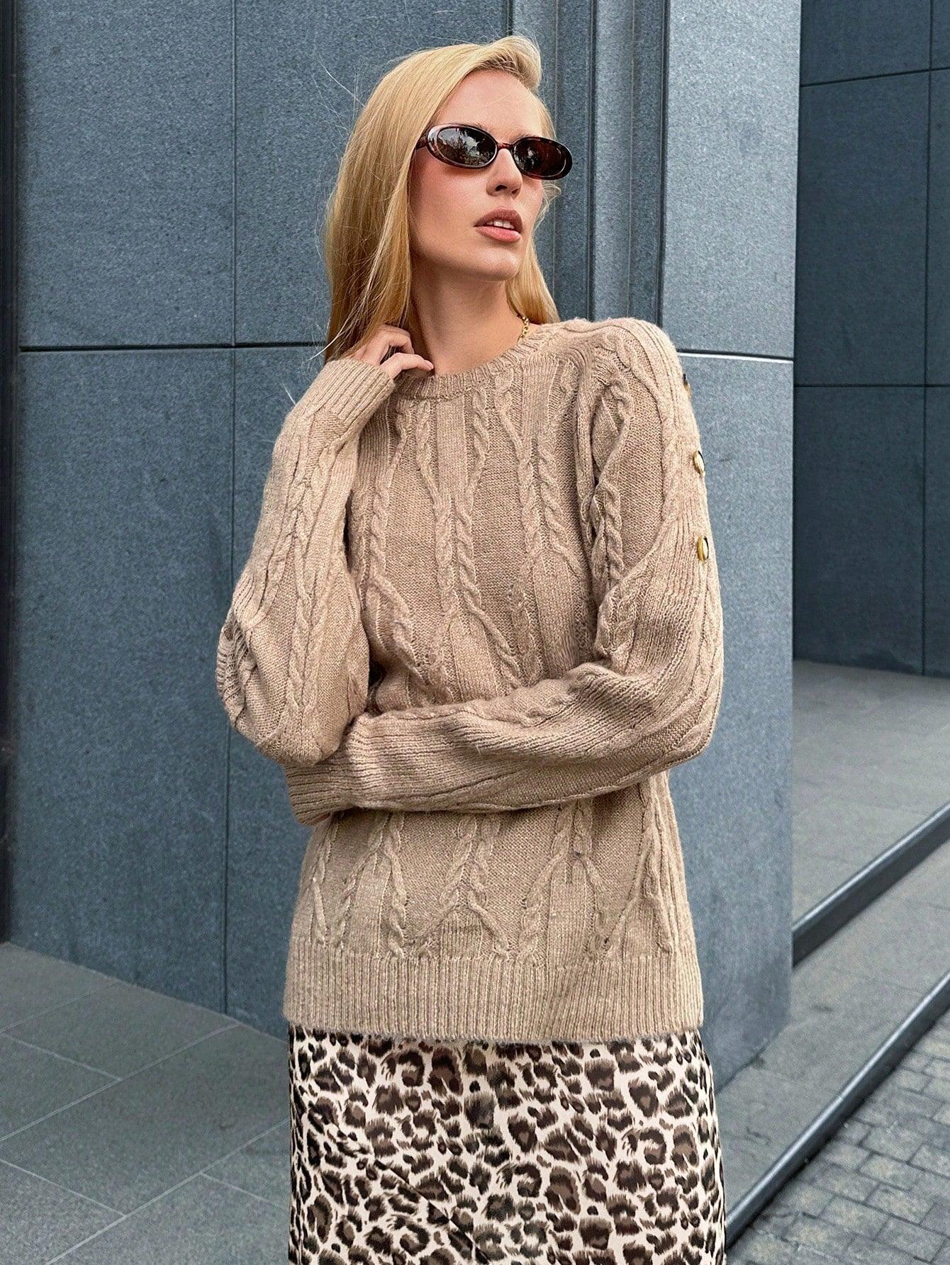 Woman wearing a tan cable knit sweater and a leopard print maxi skirt, standing outdoors.