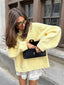 woman in a pastel yellow oversized knit sweater holding a black quilted clutch bag