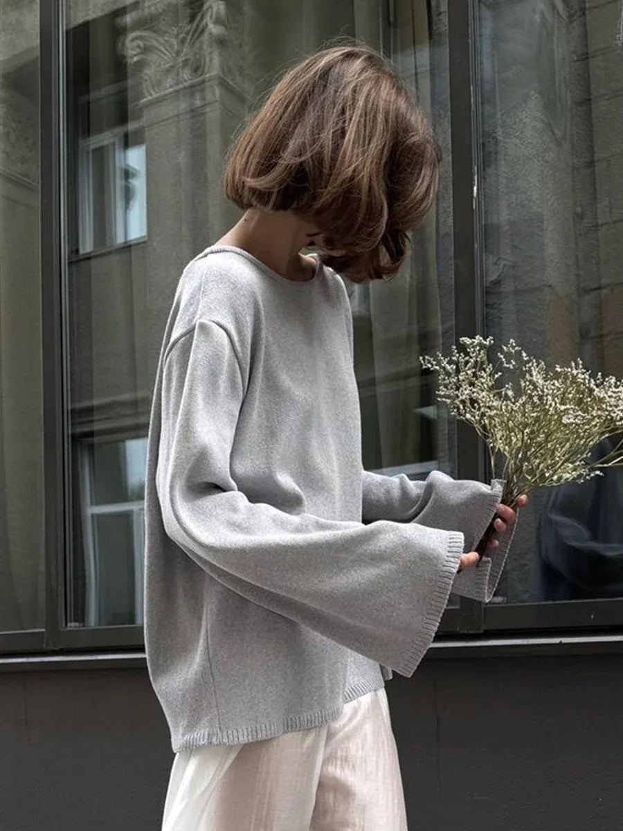 Side view of a woman in a grey oversized knit sweater with bell sleeves and a white skirt, holding dried flowers. Secondary image