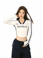 Close-up of a woman wearing a white cropped long-sleeve shirt with athletic details and navy trim.