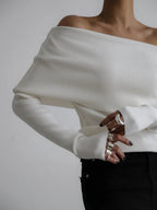 Close-up of a woman's hands wearing multiple silver rings, wearing a white off-the-shoulder sweater.