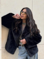 Woman wearing a black faux fur jacket over a grey top and jeans, with sunglasses.