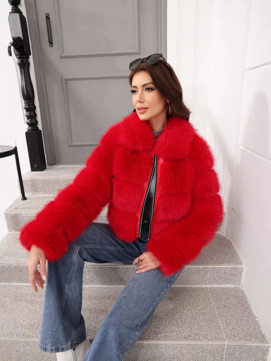 Woman wearing a red faux fur cropped jacket with a grey turtleneck and blue jeans, sitting on stairs and looking to the side.