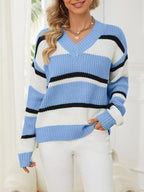 Woman wearing a blue, white, and black striped v-neck sweater with white pants.