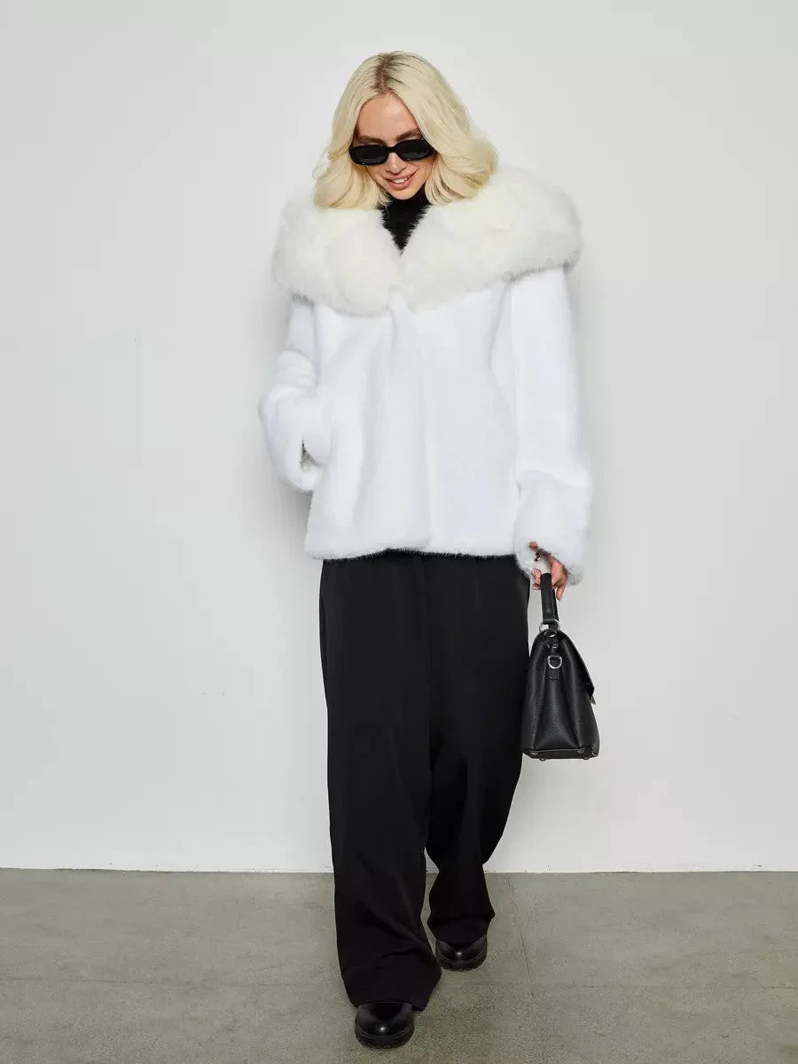 Woman wearing a white faux fur short coat over a black turtleneck and black wide-leg pants, carrying a black handbag