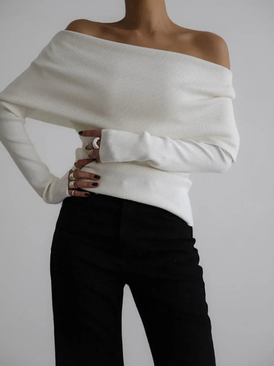 Woman wearing a white off-the-shoulder long-sleeved sweater with black pants, hands clasped in front. Main image