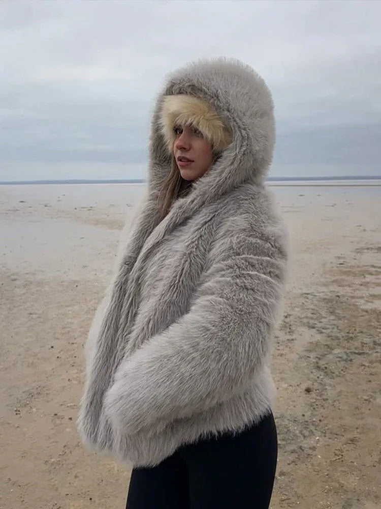 Woman standing on a beach, wearing a grey faux fur hooded coat