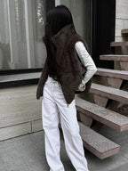 Woman wearing a brown faux fur vest over a white long-sleeved shirt and white pants, standing outdoors.