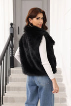 Woman wearing a black faux fur vest over a white long-sleeved shirt and blue jeans, looking over her shoulder