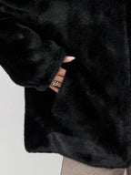 Close-up of a hand in a black faux fur jacket pocket, showing manicured nails and rings.