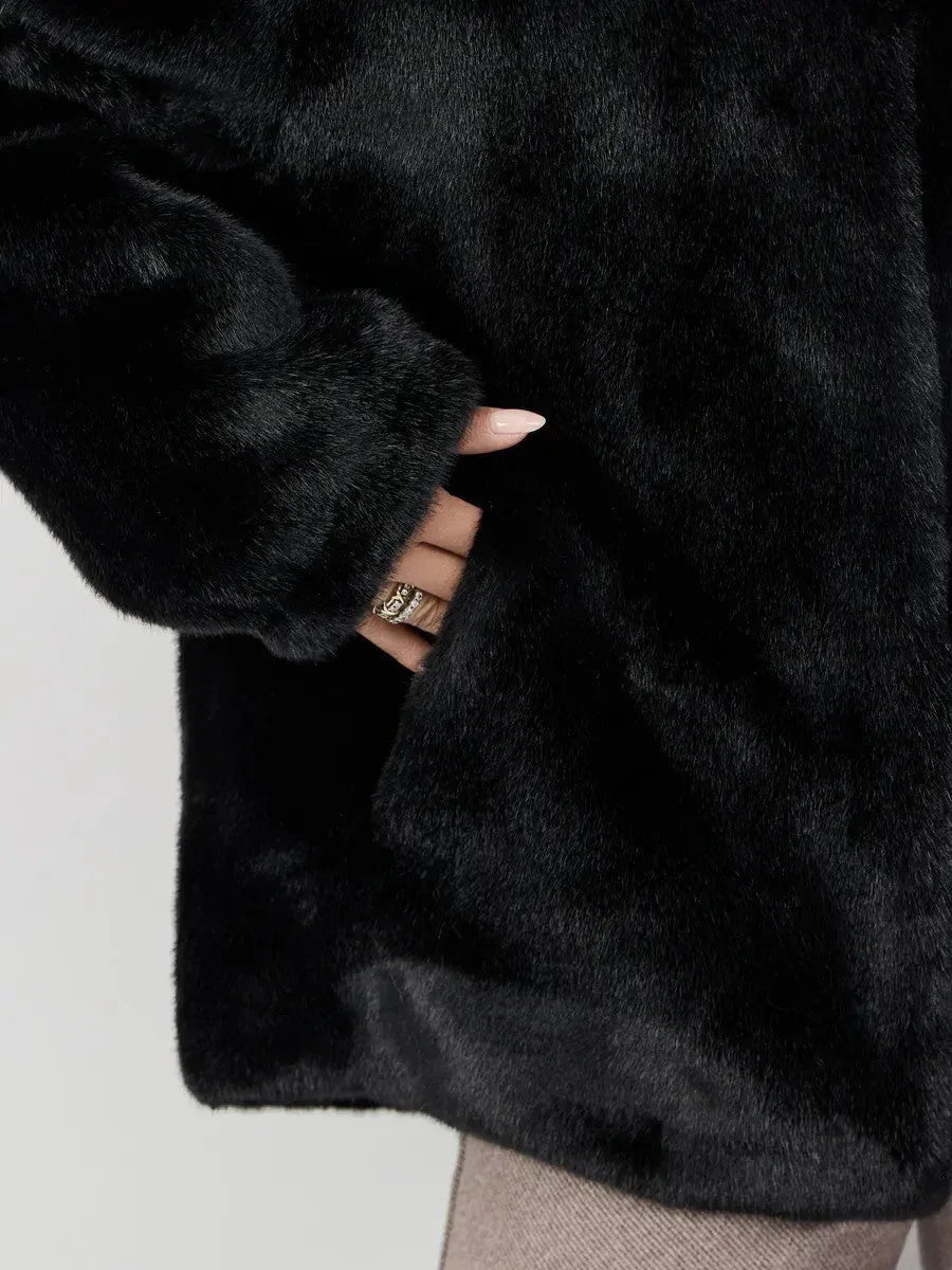 Close-up of a hand in a black faux fur jacket pocket, showing manicured nails and rings.