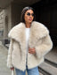 Woman in a cream-colored faux fur jacket, white top, blue jeans, and sunglasses, holding a white handbag.