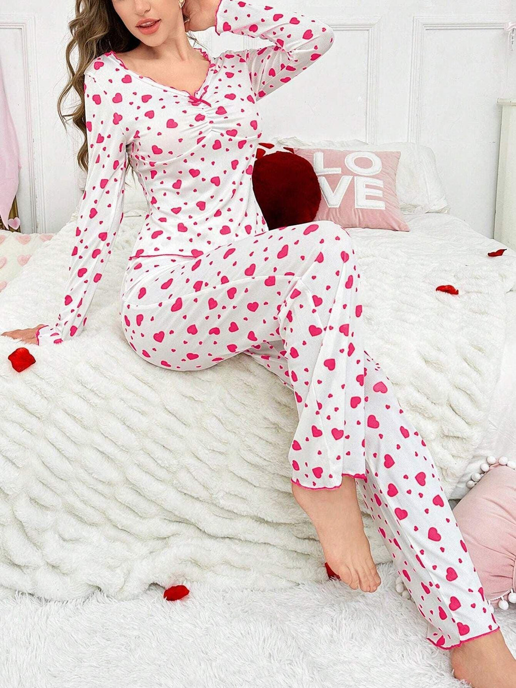 woman wearing white and pink heart print pajama set, seated on bed, medium shot