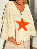 Woman with hands in pockets wearing an off-white knitted sweater with an orange star graphic