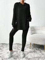 Woman posing in a black ribbed knit loungewear set with a hooded tunic and leggings.
