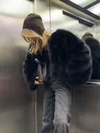 Woman in an elevator wearing a black faux fur jacket, beanie, and studded jeans