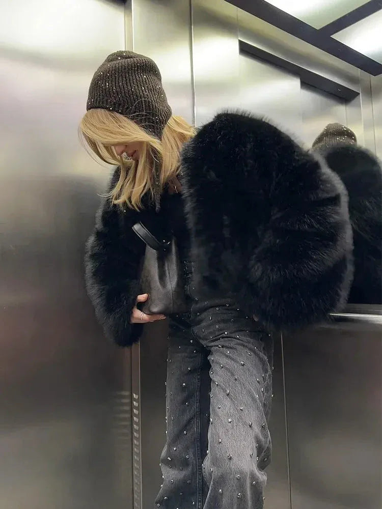 Woman in an elevator wearing a black faux fur jacket, beanie, and studded jeans